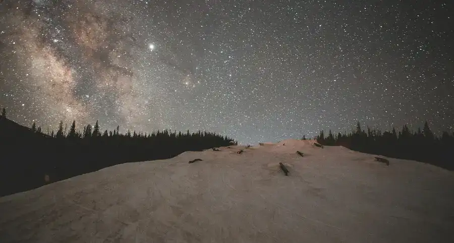 Copper Mountain, Frisco, USA, and the majestic Milky Way Galaxy stretching across a night sky above a snow-covered landscape with a forest in the background.